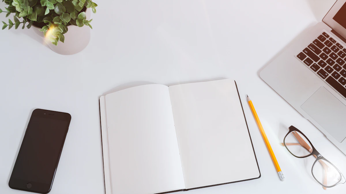 An open notebook beside a phone and laptop on a white desk